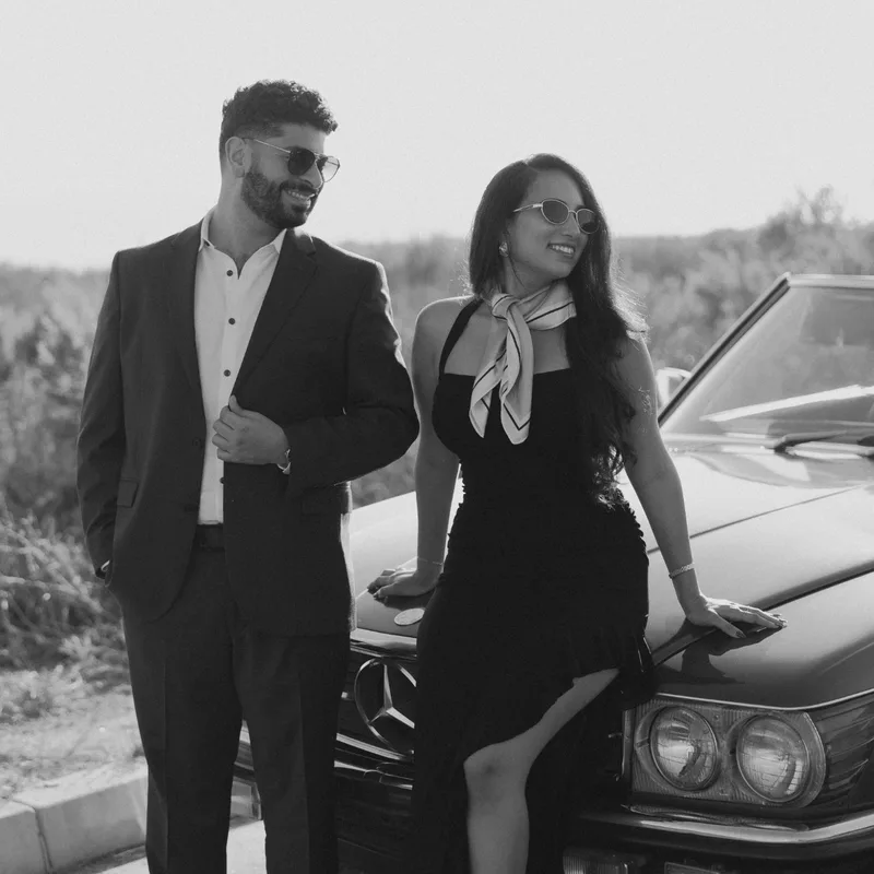 Black-and-white photo of David and Joy smiling against the hood of the vintage Mercedes