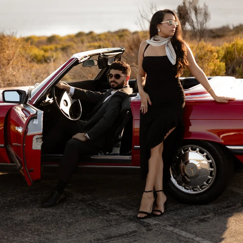 David and Joy with a vintage Mercedes convertible on a coastal bluff, the ocean behind them